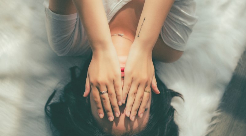 Woman hands over face in distress with arrow tattoo