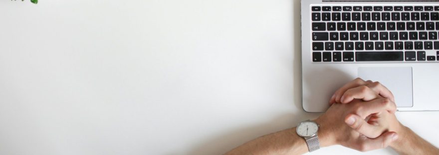 two hands clasped with watch on top of open laptop keyboard.