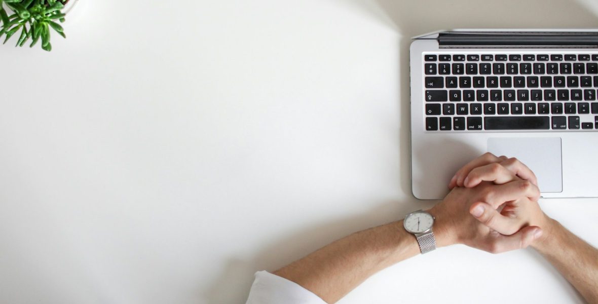 two hands clasped with watch on top of open laptop keyboard.